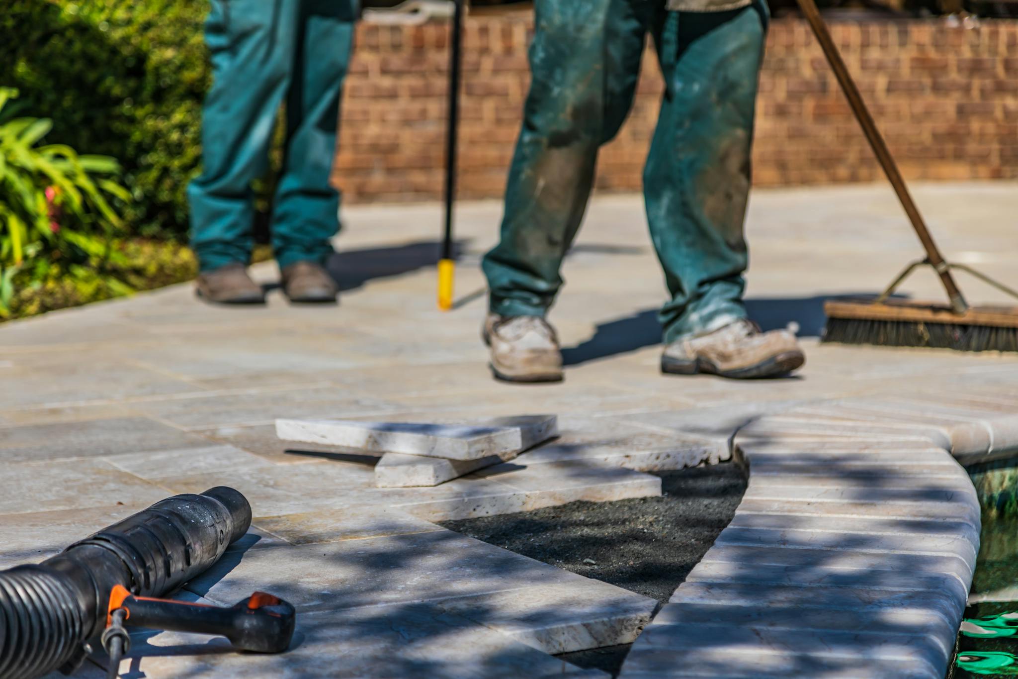 Workers laying tiles on an outdoor patio under sunlight.